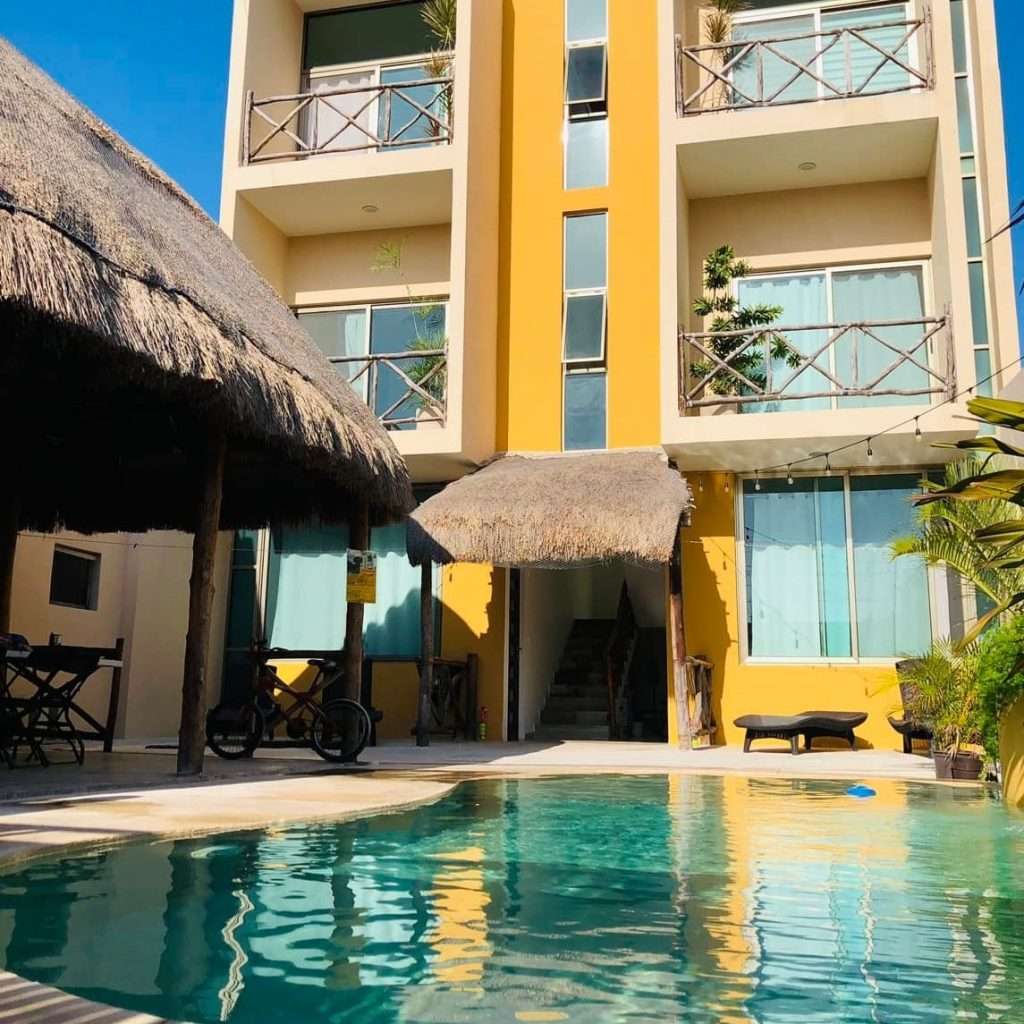 Fachada de varios pisos con alberca y palapa de Hotel El Muelle