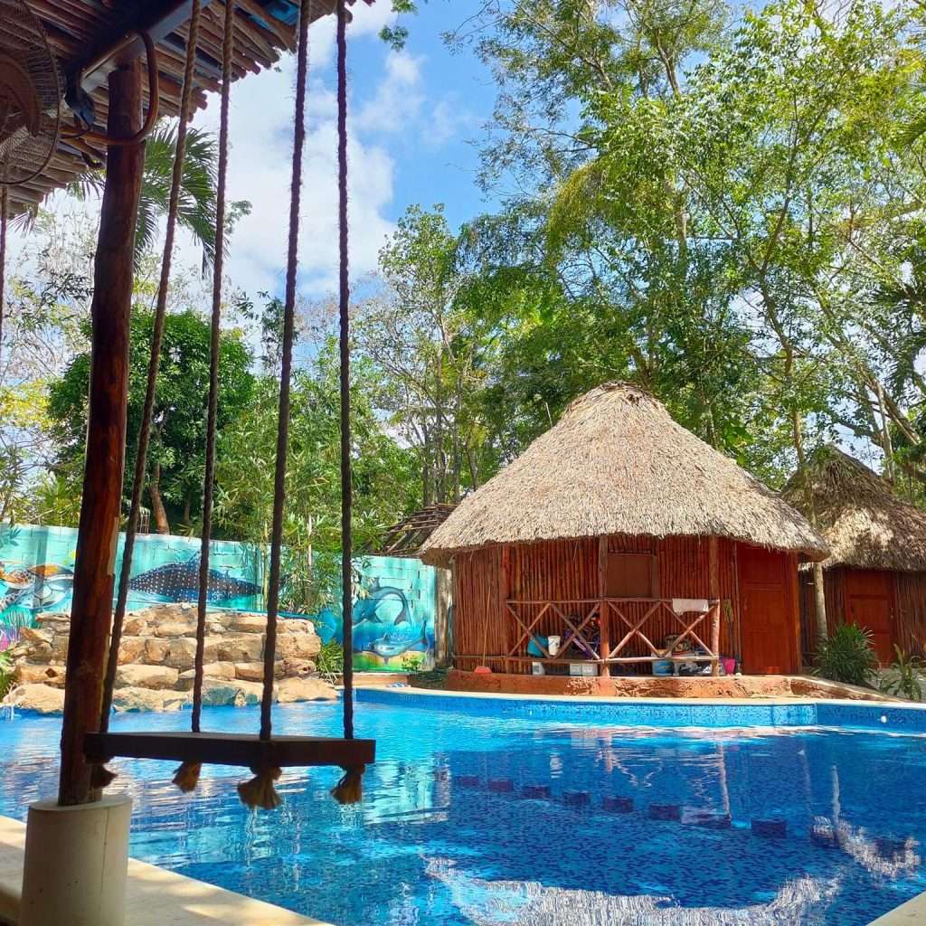 alberca con columpio y 2 palapas tipo maya de fondo